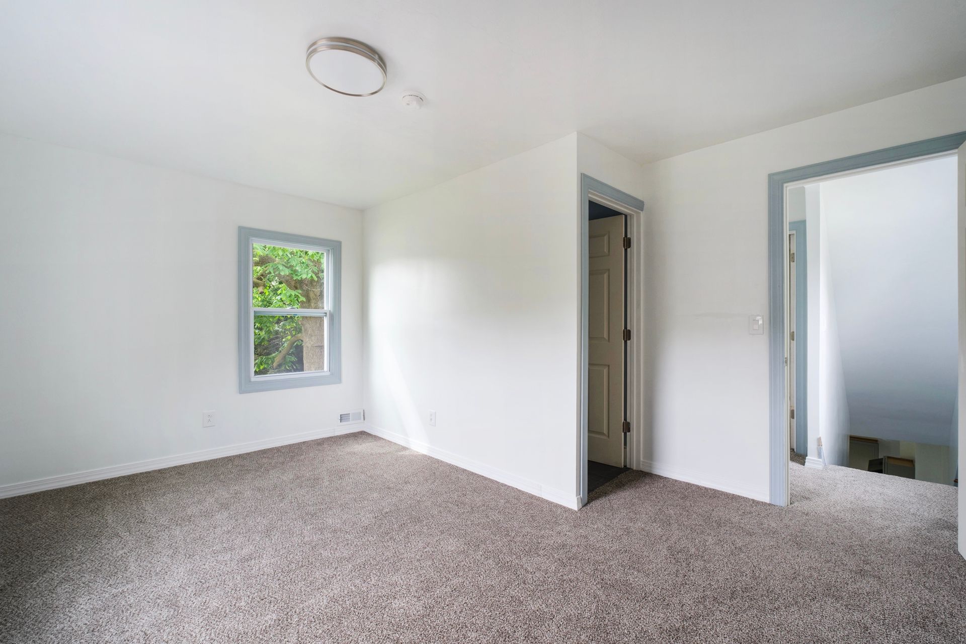 An empty bedroom with a carpeted floor , white walls and a window.