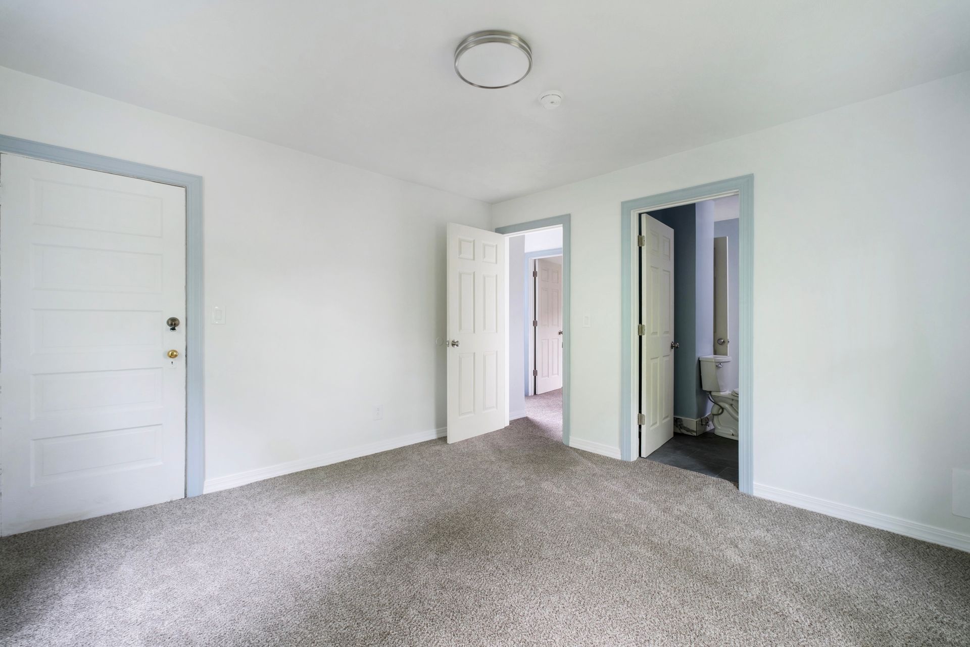 An empty bedroom with a carpeted floor and a toilet.