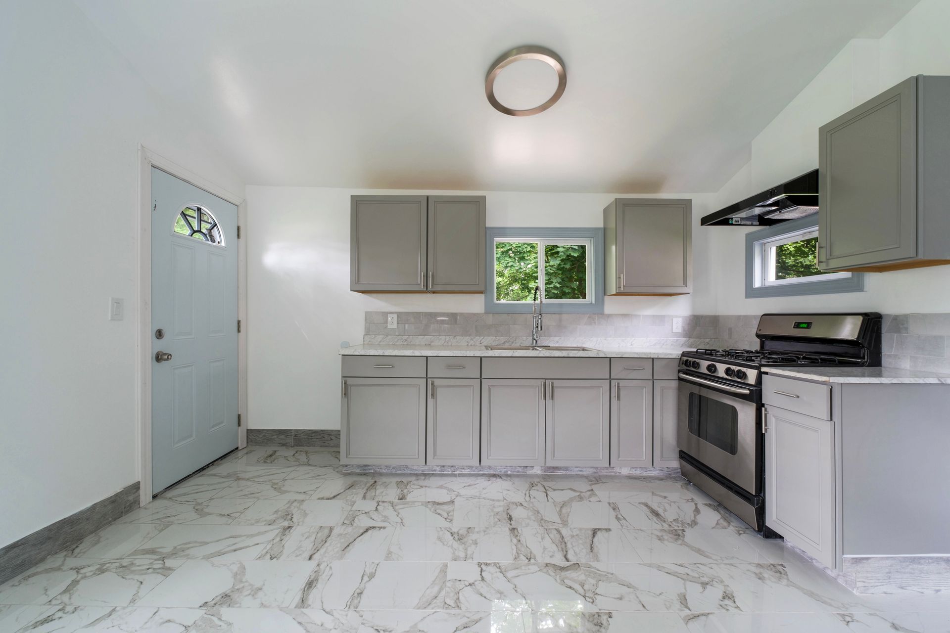 A kitchen with a stove , sink , cabinets and marble floor.