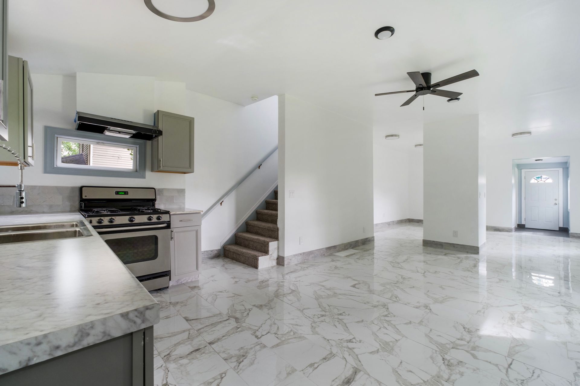 A kitchen with a stove , sink , stairs and a ceiling fan.