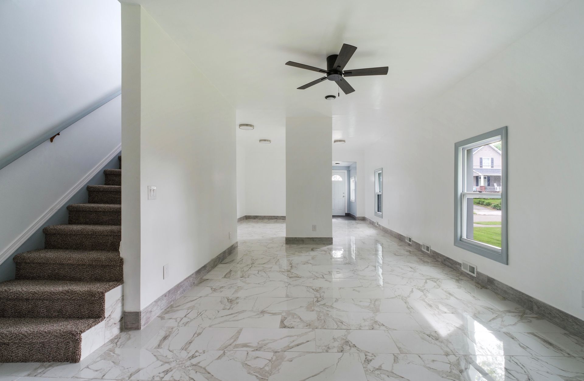 An empty living room with stairs and a ceiling fan.