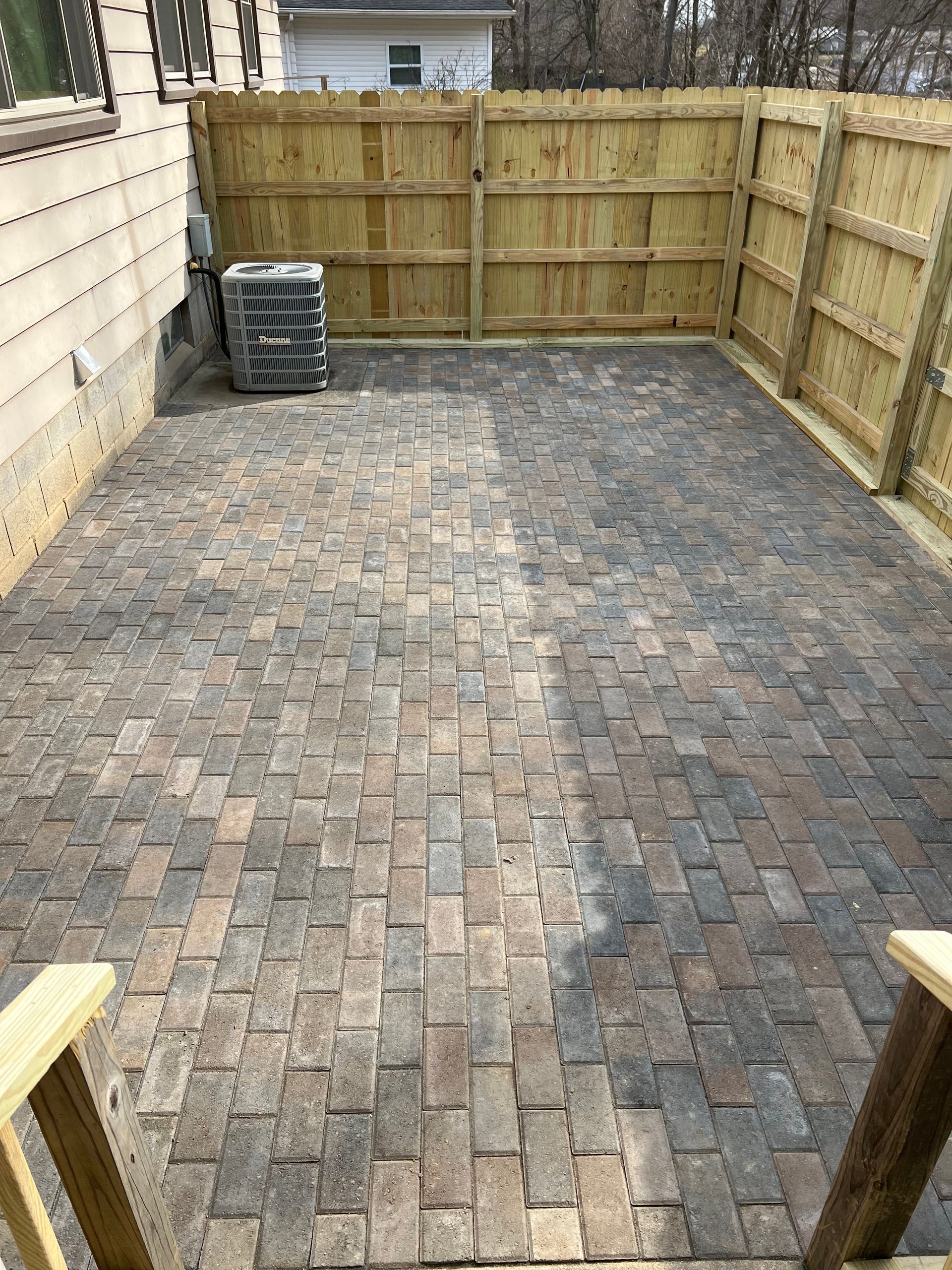 A brick patio with a wooden fence and a wooden air conditioner.