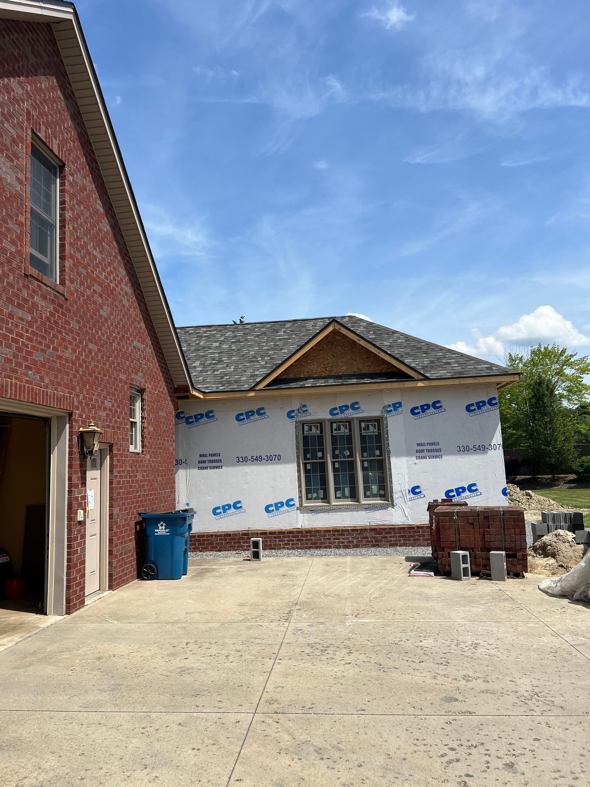 A brick house is being remodeled with a blue trash can in front of it.