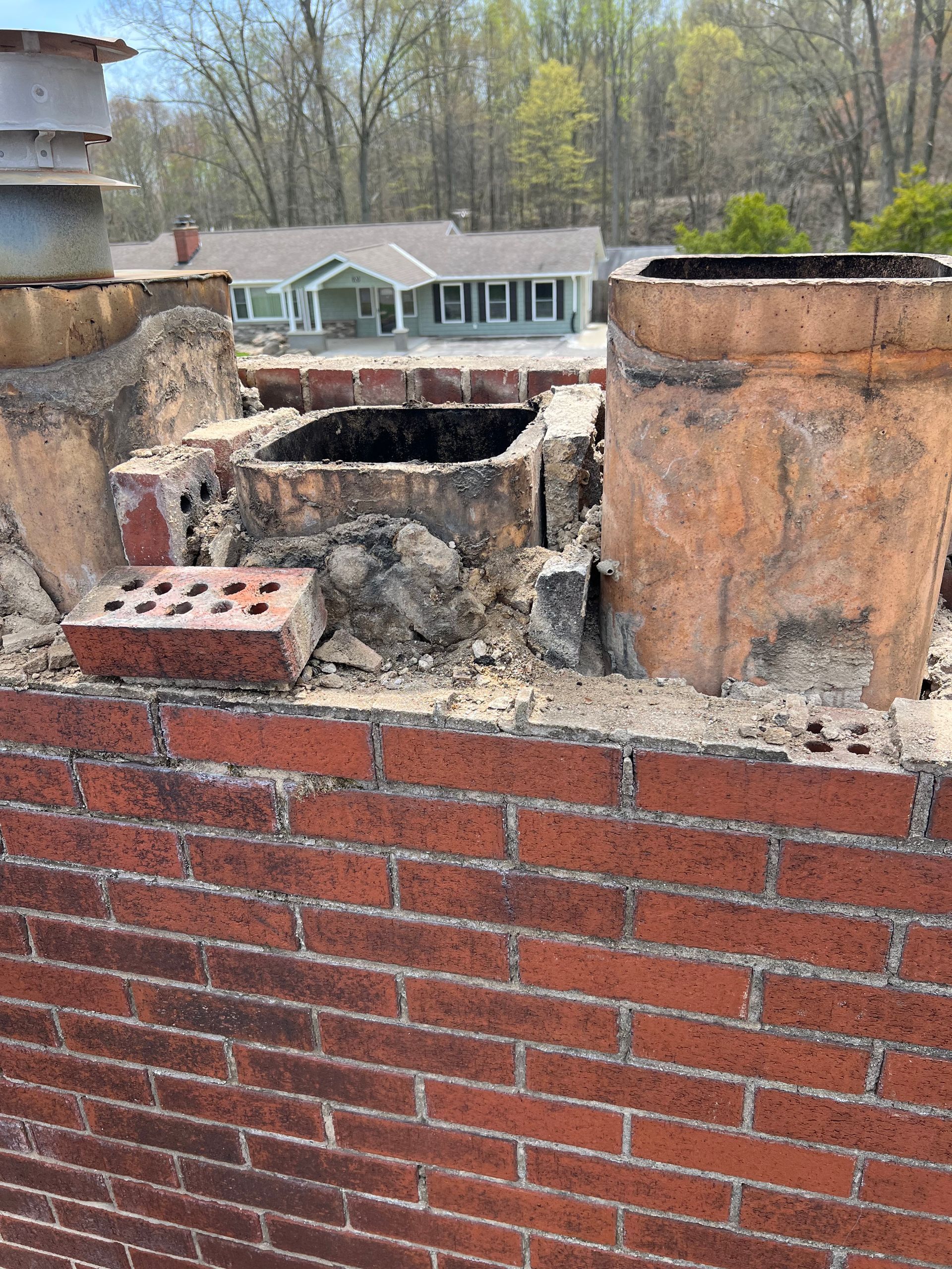 A brick chimney with a hole in it and a house in the background.