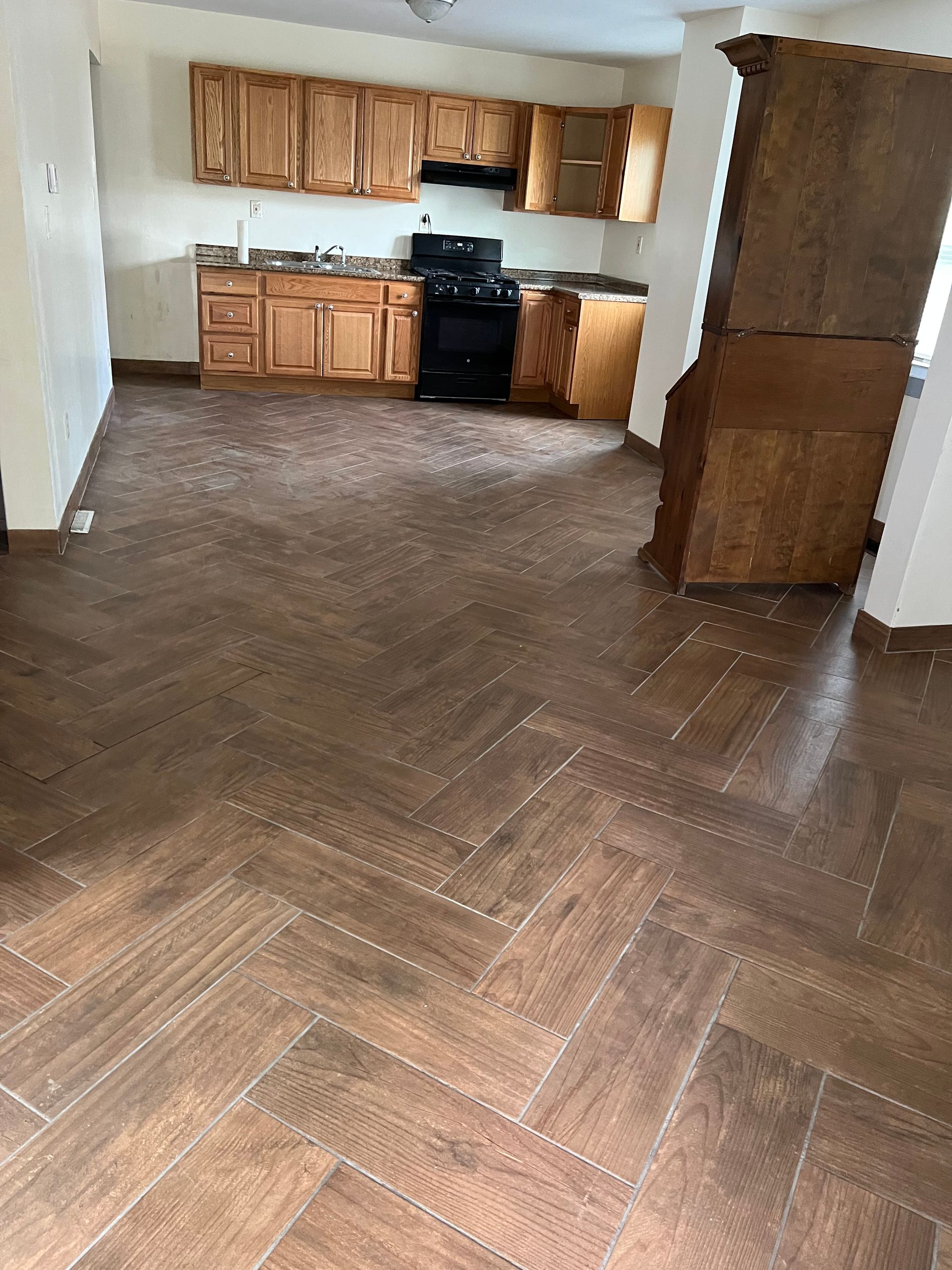 A kitchen with wooden cabinets , a stove , and a herringbone tile floor.