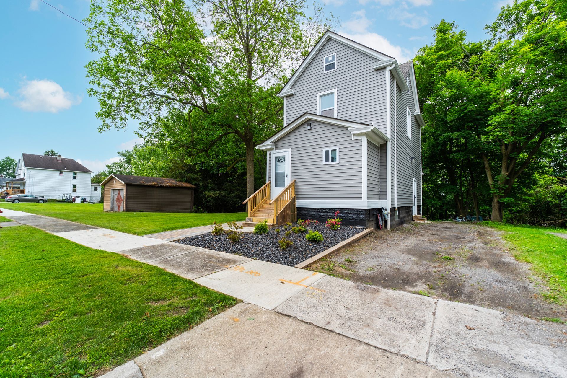 A house with a concrete walkway leading to it is surrounded by trees and grass.
