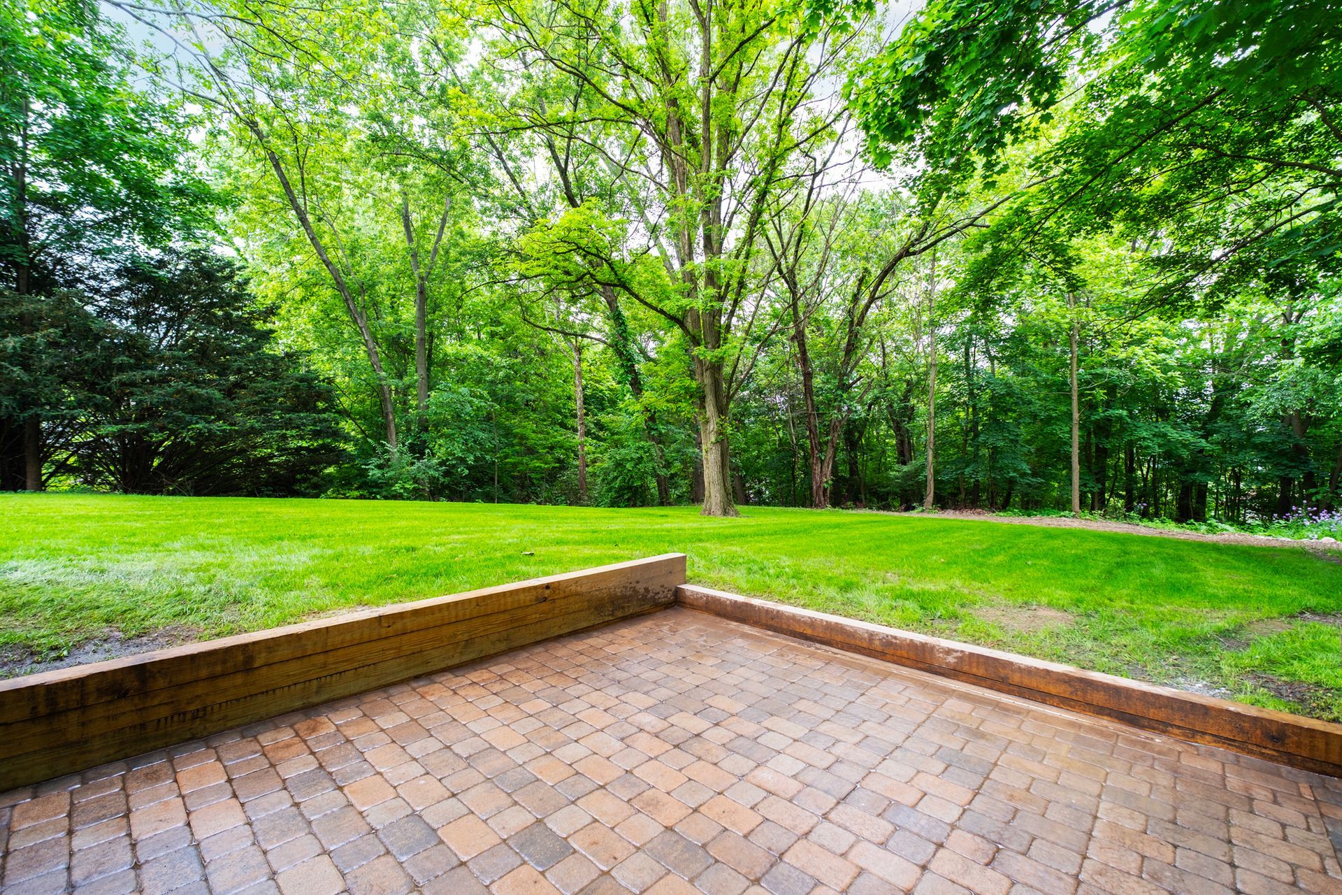 There is a brick patio in the middle of a lush green park.