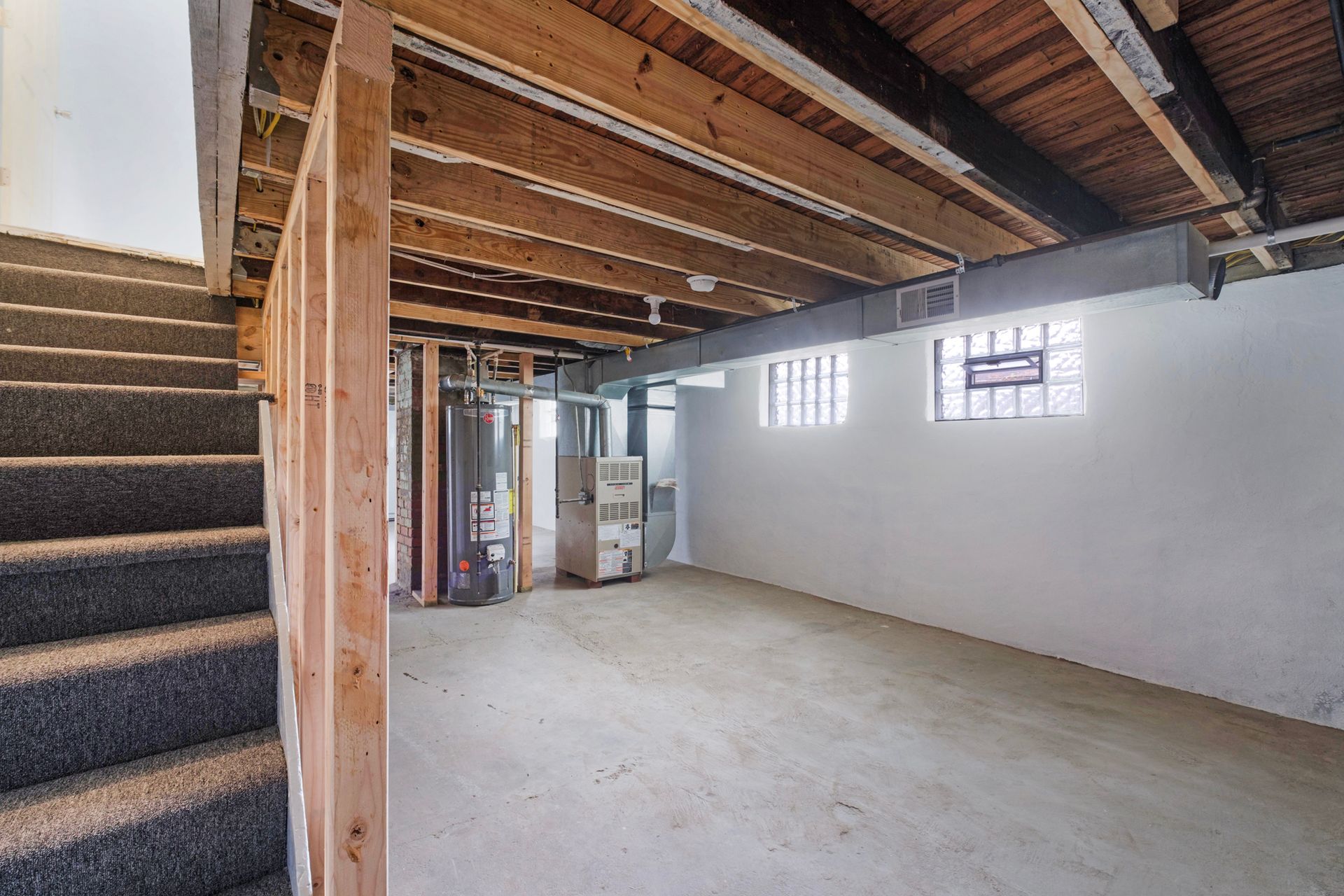 An empty basement with stairs and a wooden ceiling.