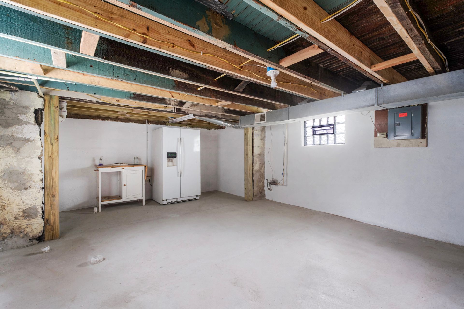 An empty basement with a refrigerator and a window.