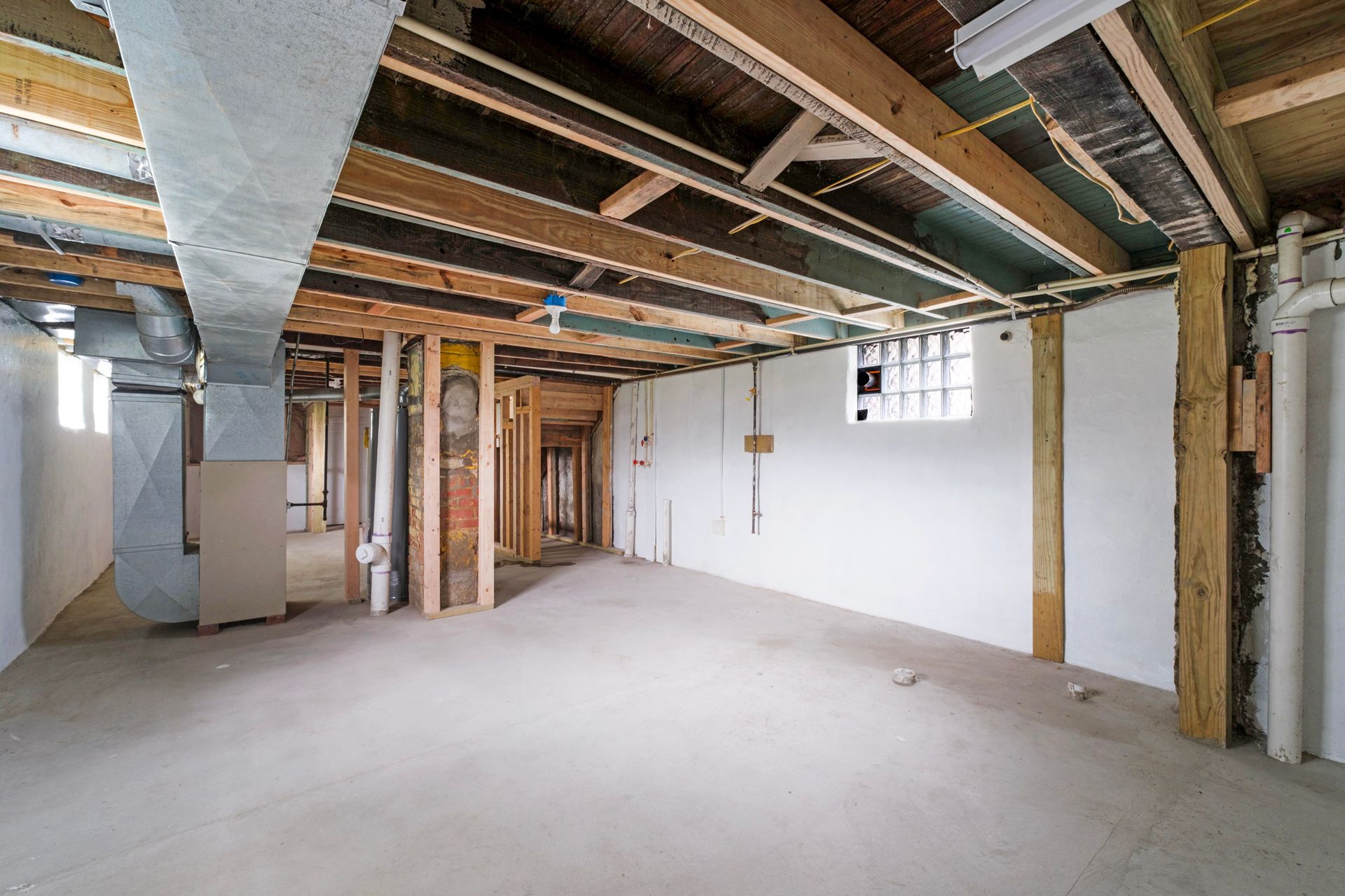 An empty basement with wooden beams and a window.