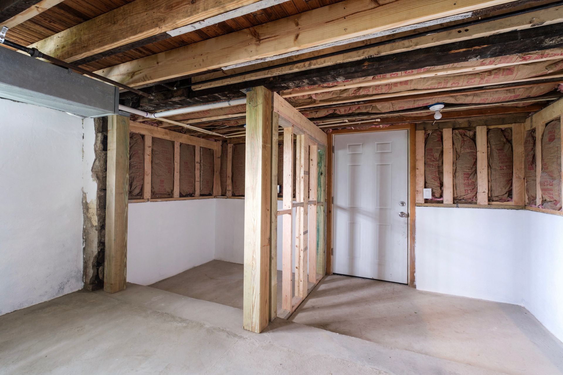 An empty basement with wooden beams and a door.