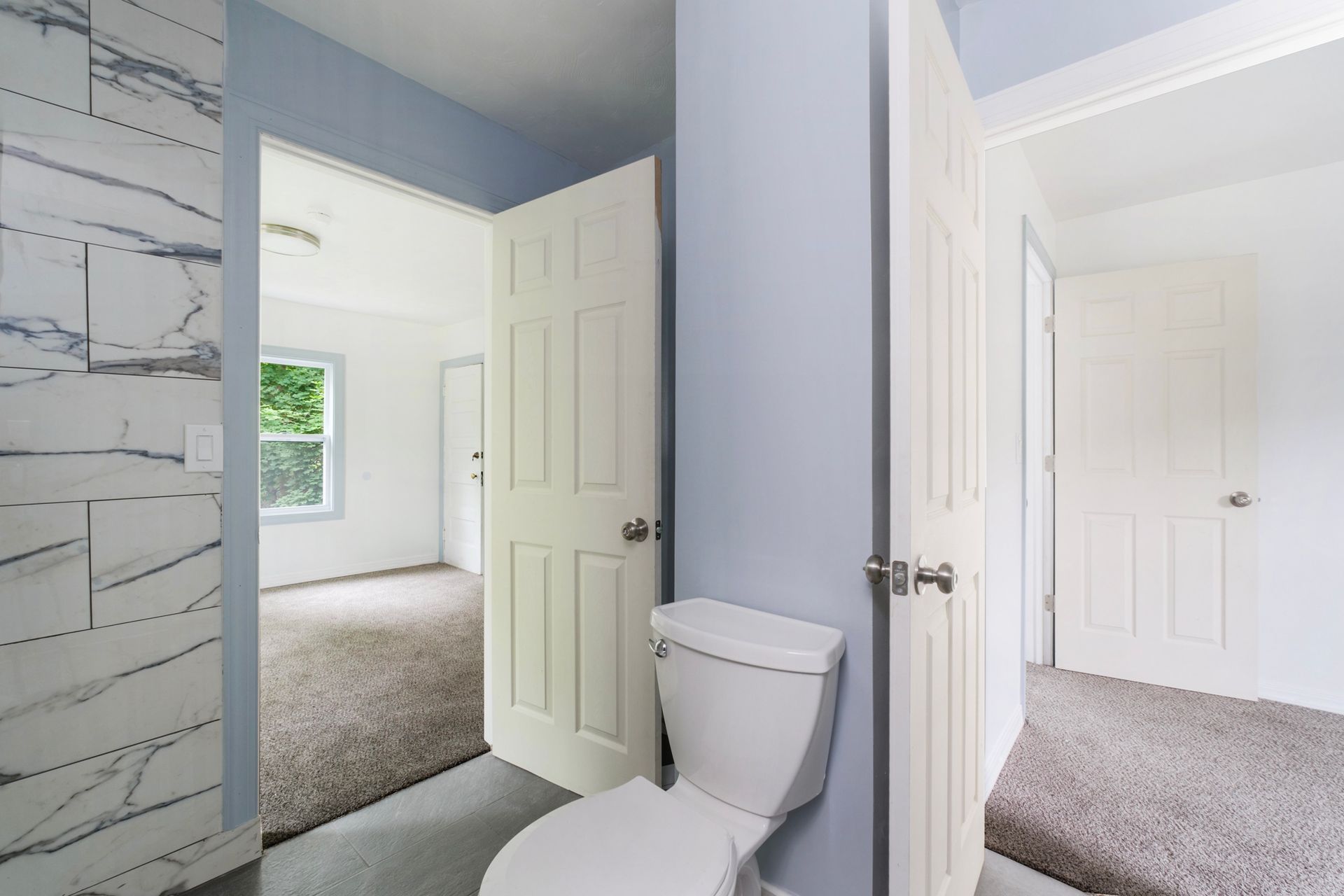 A bathroom with a toilet and a bedroom in the background.