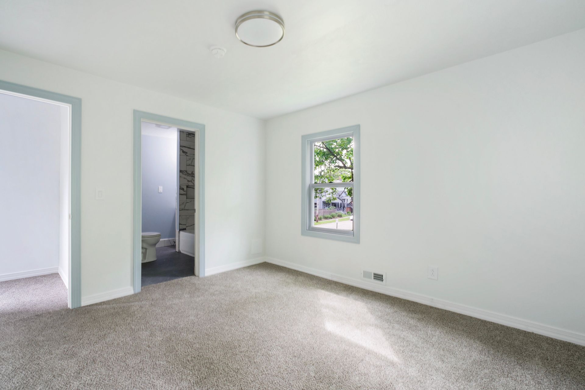 An empty room with a window and a carpeted floor.