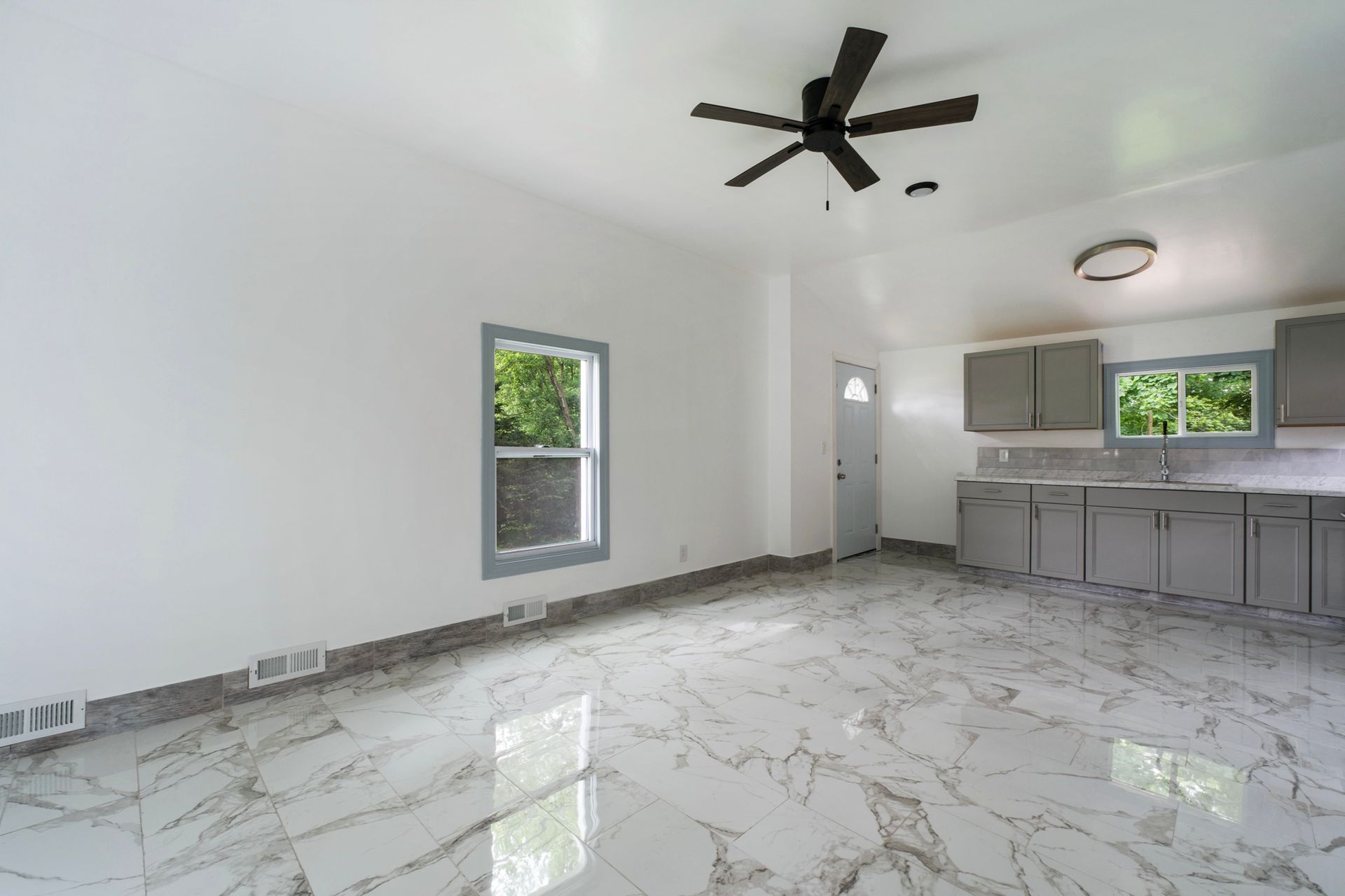 A living room with a ceiling fan and a kitchen in the background.