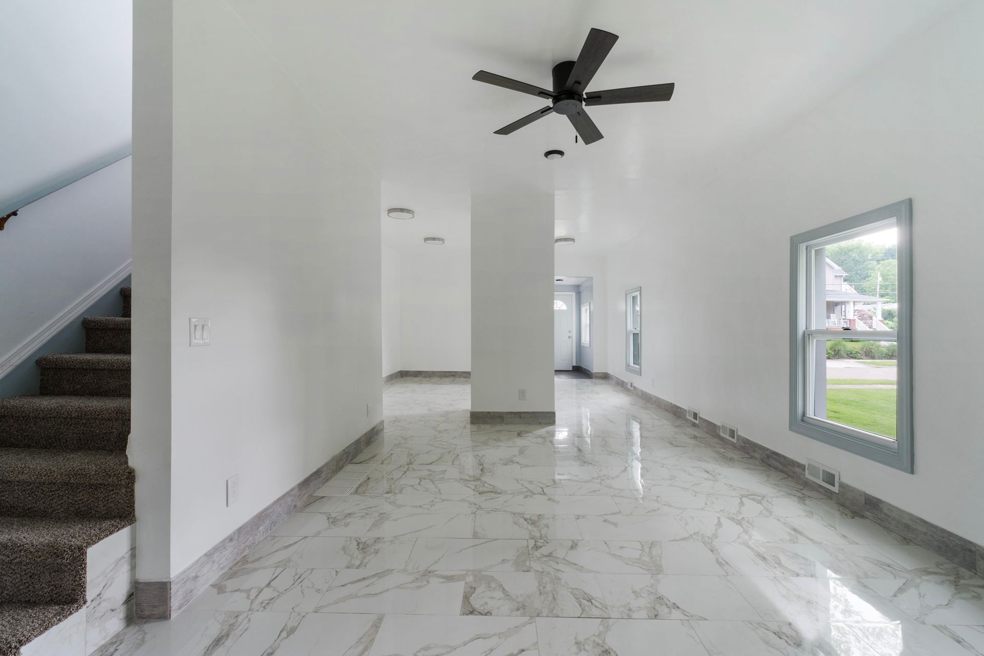 An empty living room with a ceiling fan and stairs.