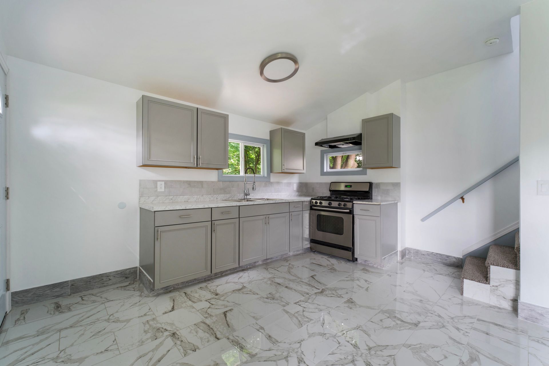 A kitchen with a stove , sink , cabinets and stairs.