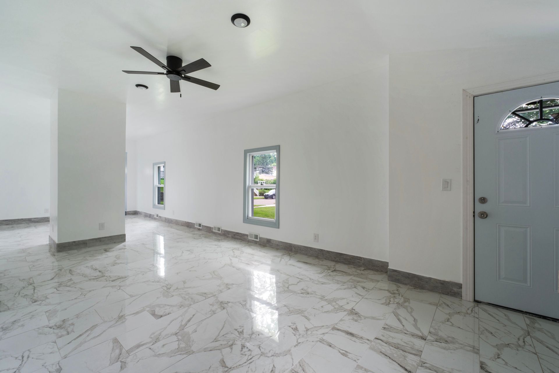 An empty living room with a ceiling fan and marble floors.