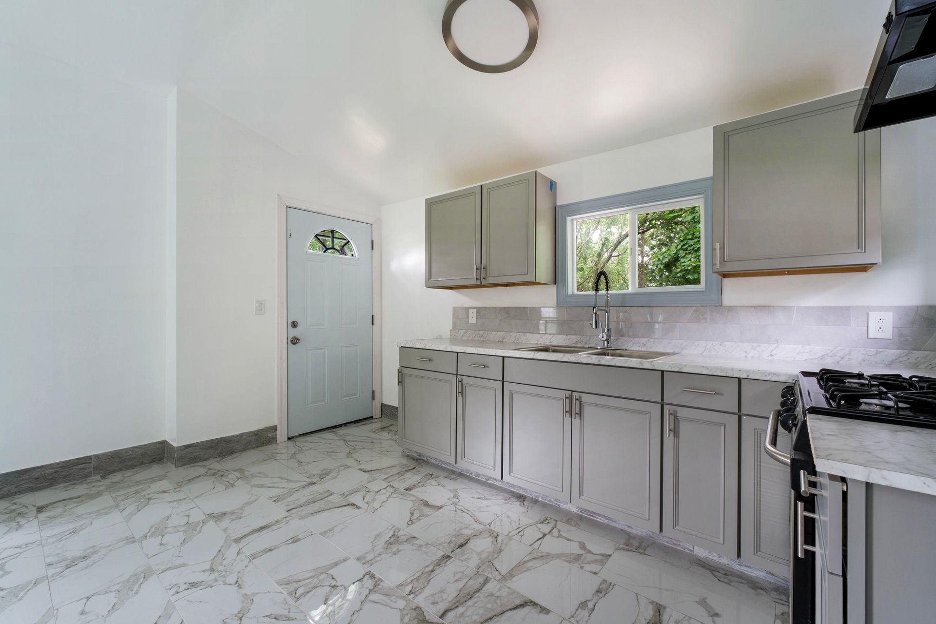 A kitchen with gray cabinets , a stove , a sink , and a window.