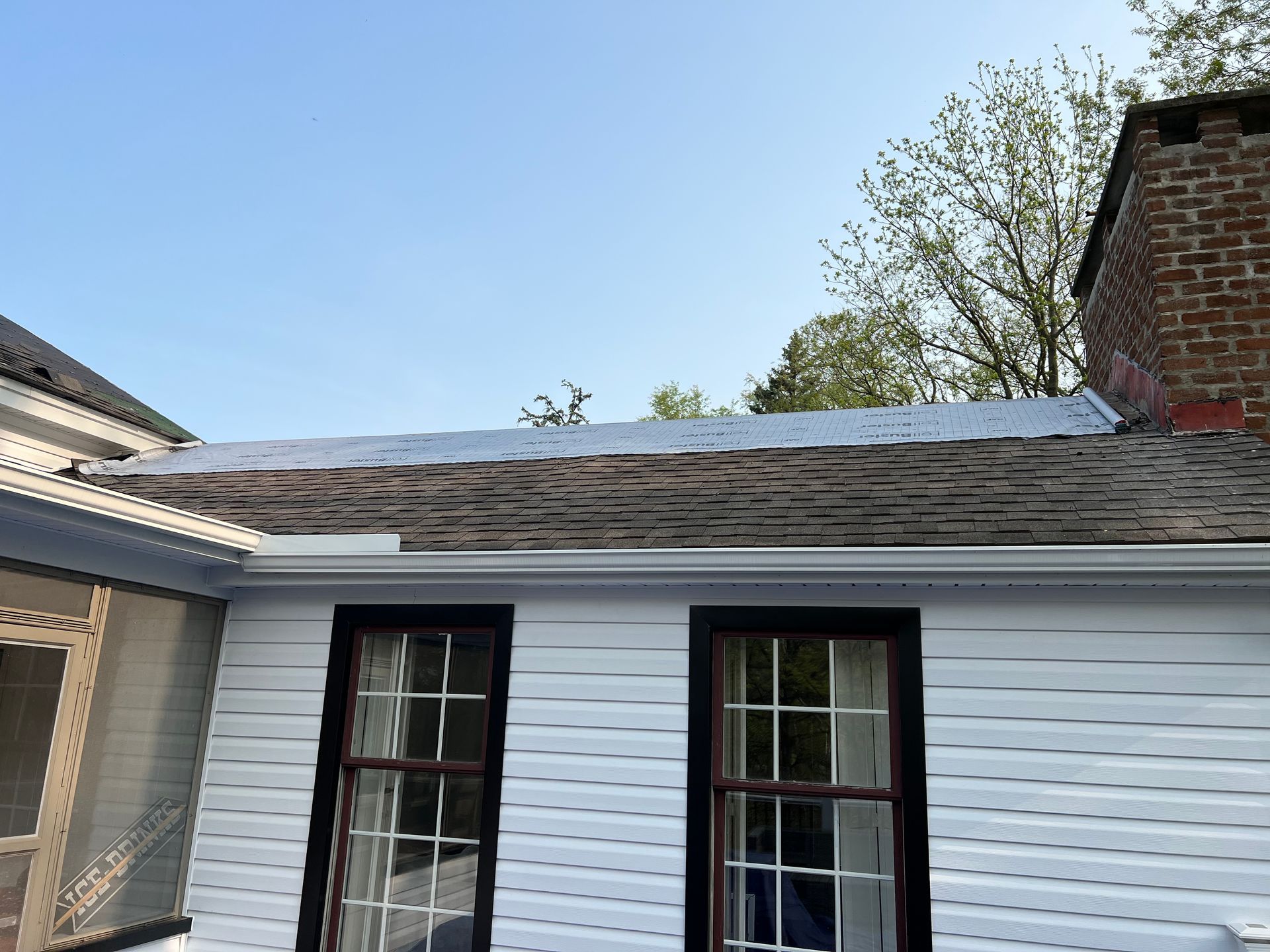 A white house with two windows and a roof that is missing shingles.