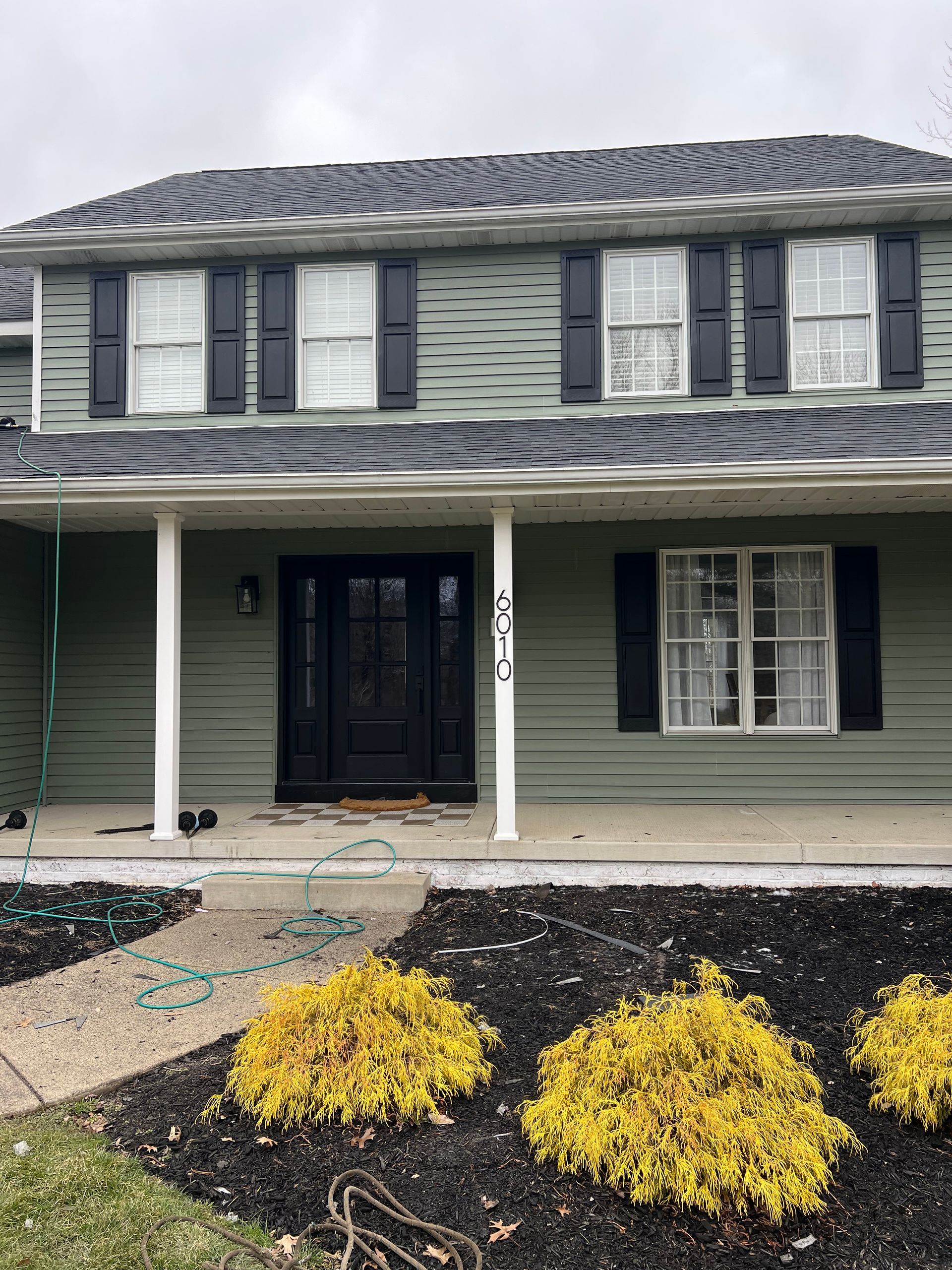 A green house with black shutters and a porch.