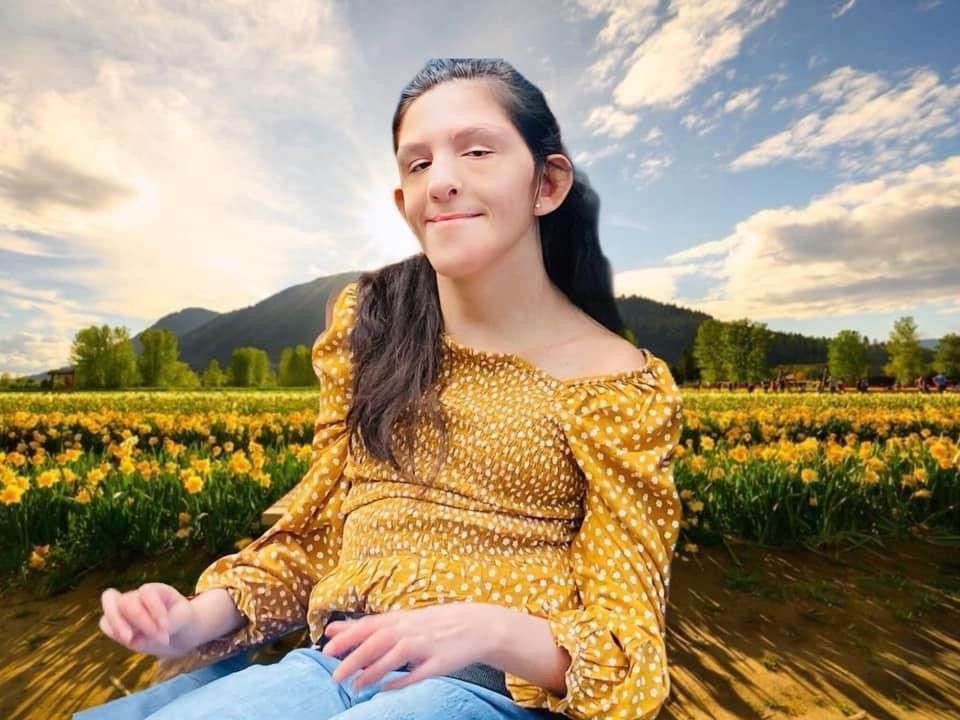Woman in yellow top smiles in a daffodil field against a mountain backdrop.