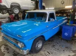 Bright blue classic pickup truck, white roof, parked in garage bay.