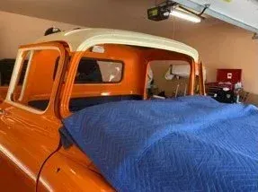 Orange and white vintage pickup truck in a garage, covered with a blue blanket.