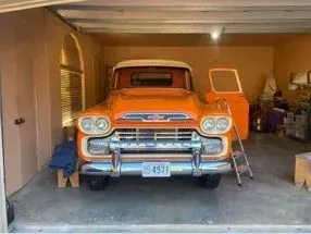 Orange vintage GMC truck parked in a garage, door open.