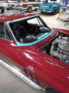 Red classic Corvette with new windshield being worked on in a garage.