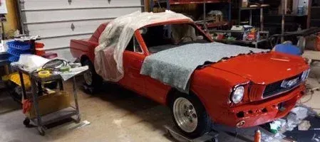 Red classic Mustang car being worked on in a garage.