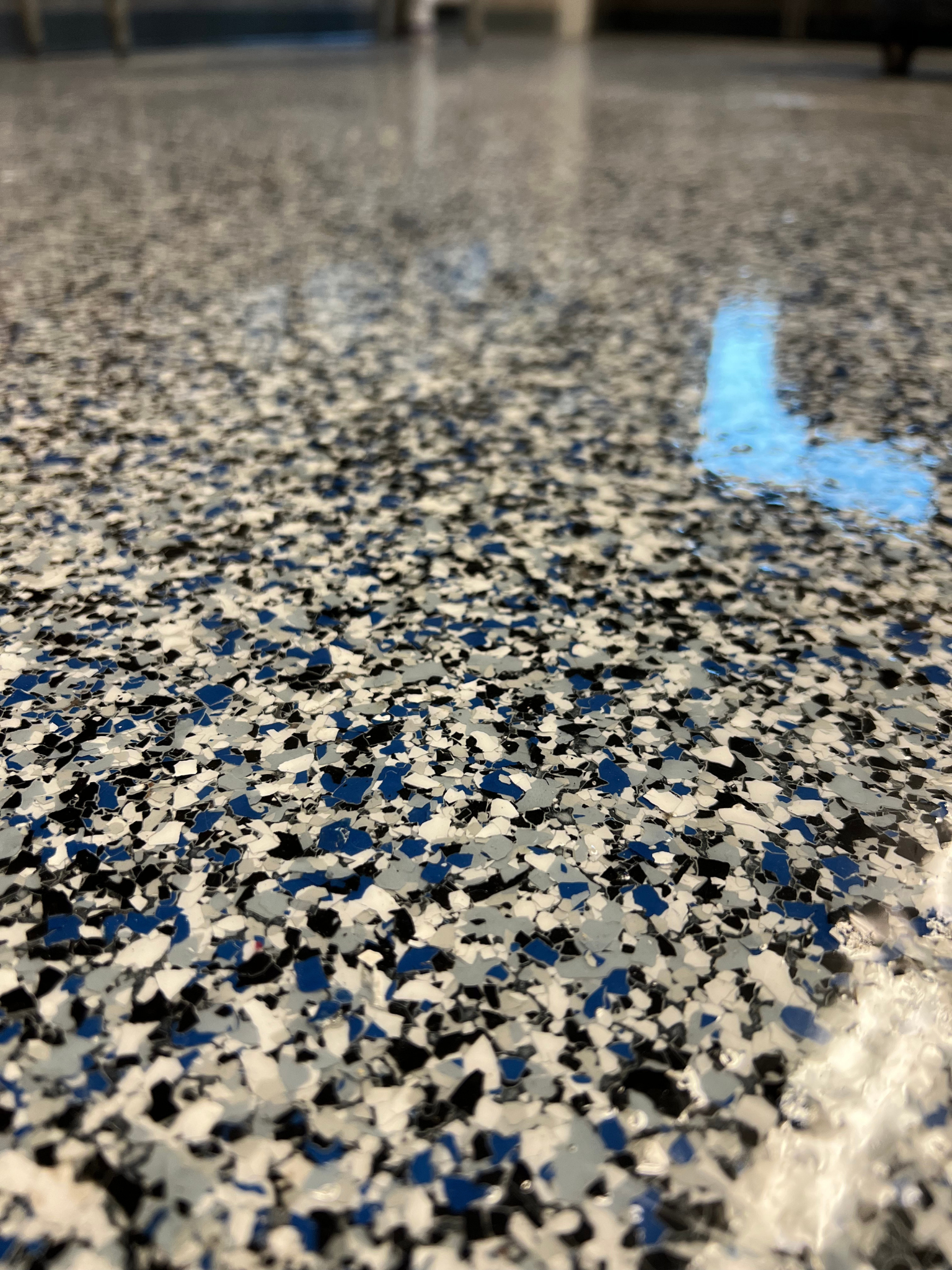 Close-up of speckled terrazzo floor with a blue painted marking and blurred hallway in the background