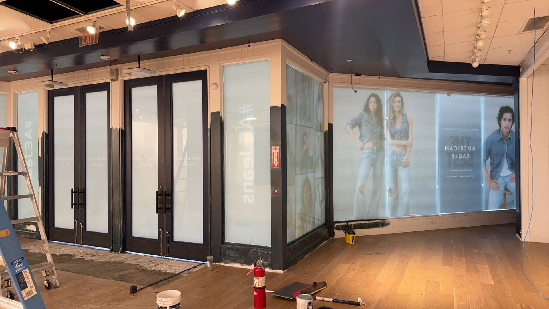 Empty storefront with glass doors, storefront posters, and construction materials on the floor at night.