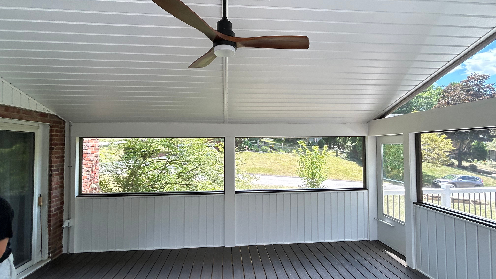 Covered porch with white railing, ceiling fan, and screened openings overlooking trees and a driveway