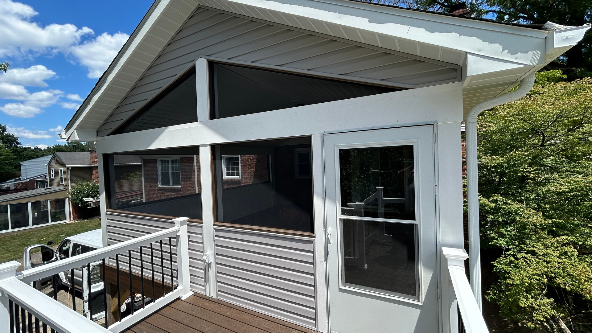 White house porch with railing, gray siding, large windows, and a sloped roof under a blue sky
