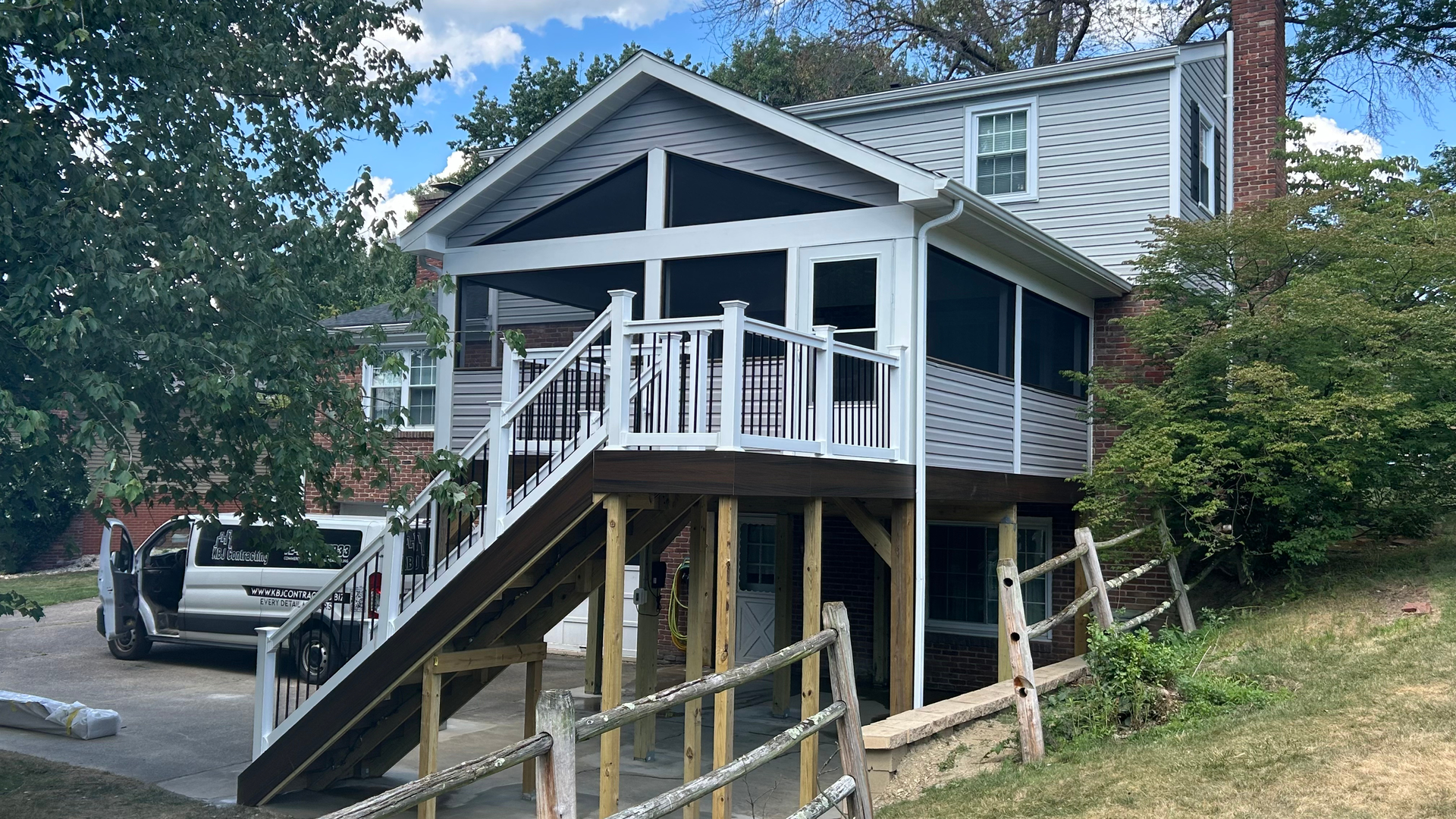 Elevated house with front porch and stairs, parked truck at left, on a wooded hillside driveway