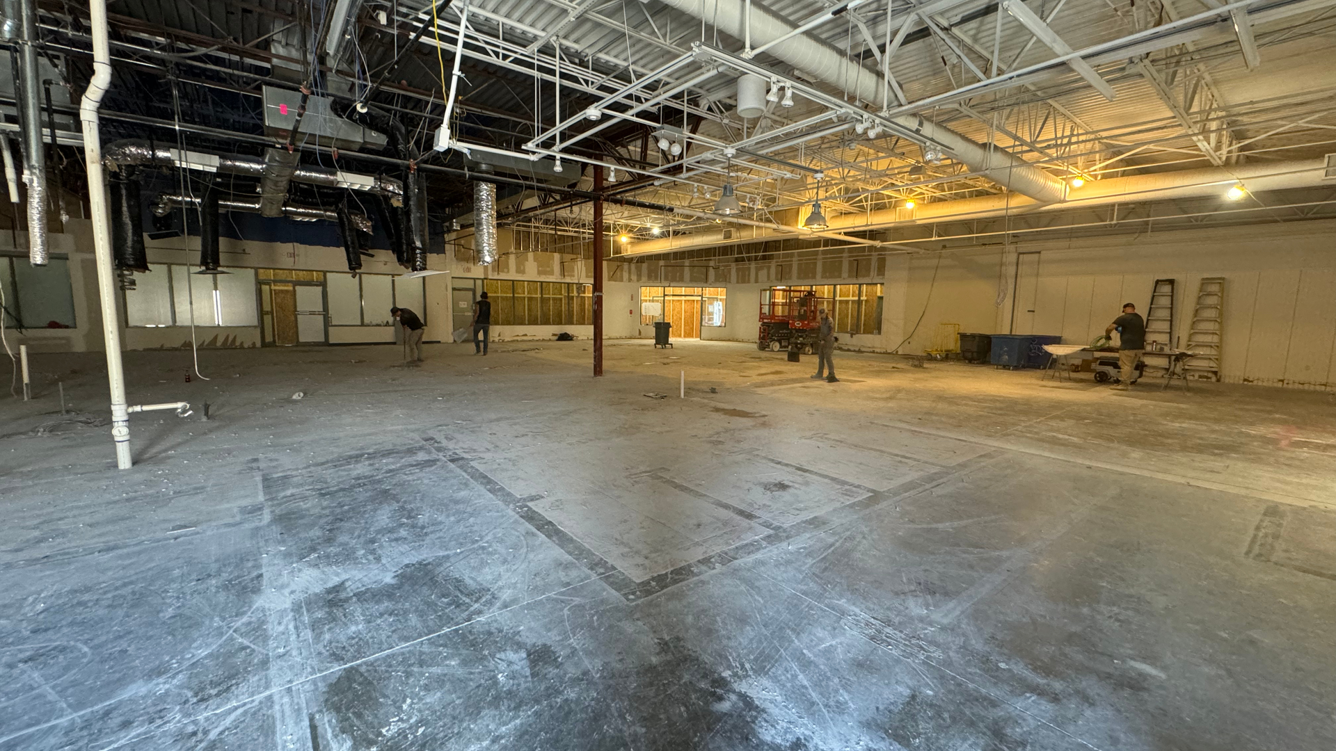 Empty unfinished industrial interior with exposed ceiling, concrete floor, and construction materials scattered around