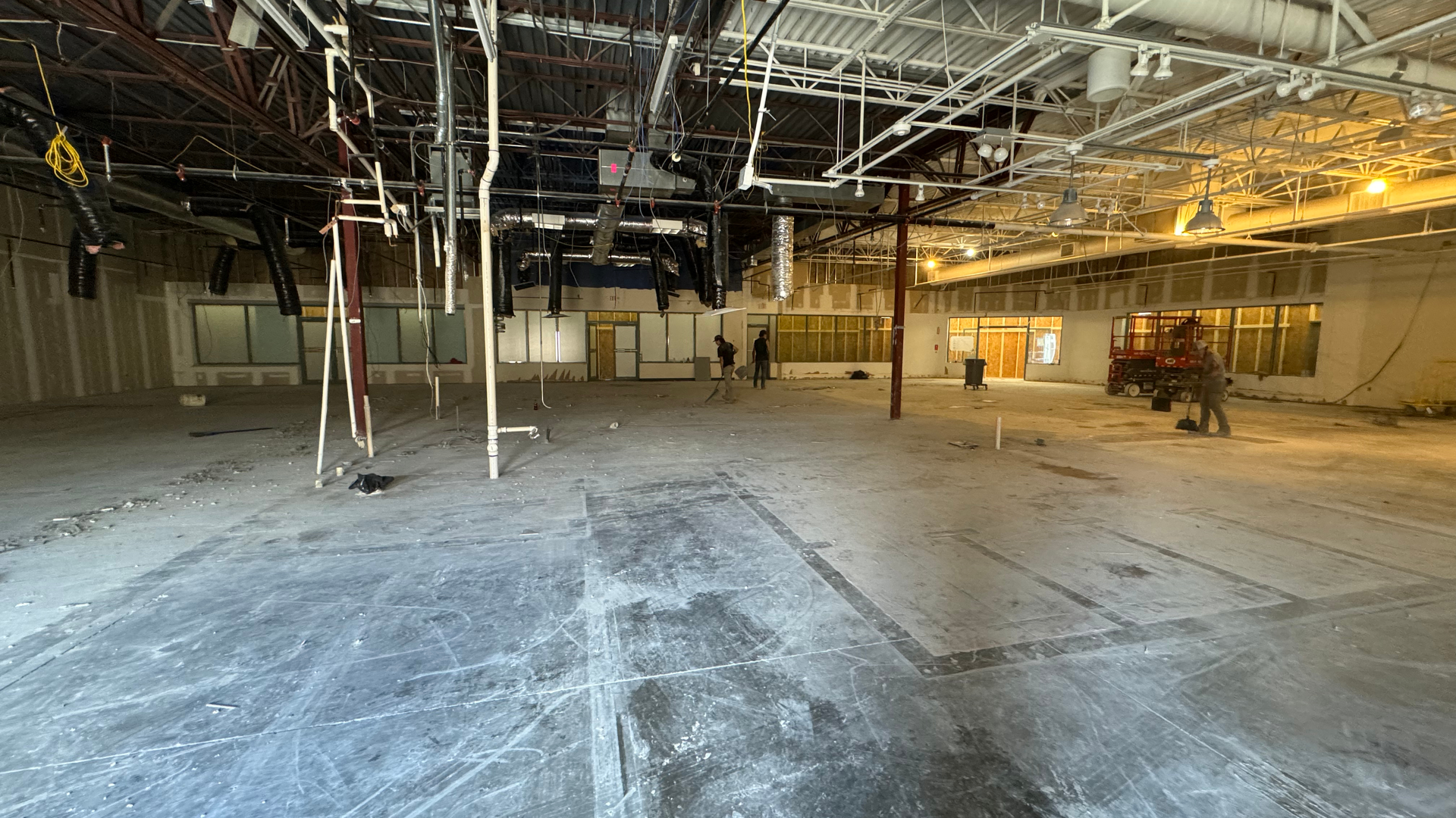 Empty unfinished warehouse interior with exposed ceiling beams, hanging wires, and concrete floor