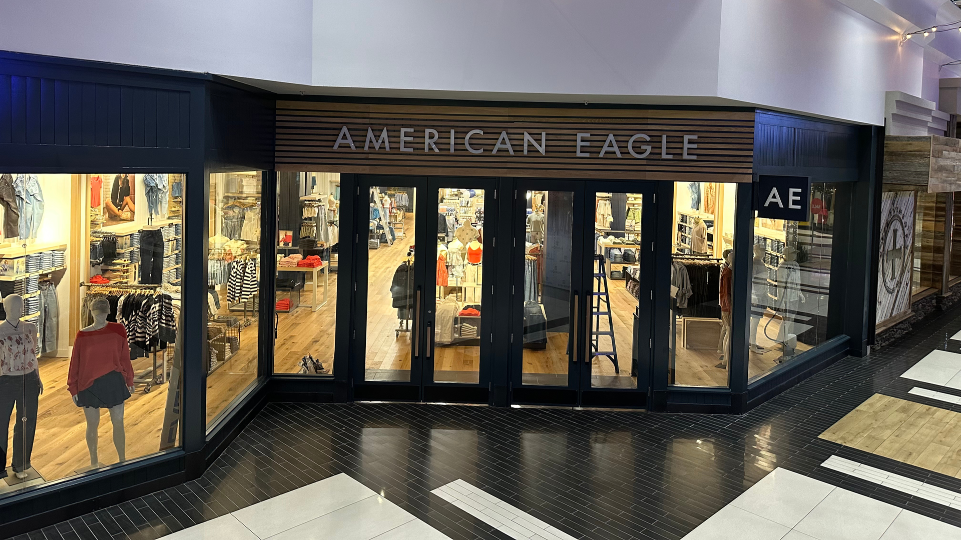 American Eagle storefront in a mall, with black-framed glass doors and a lit clothing display inside.