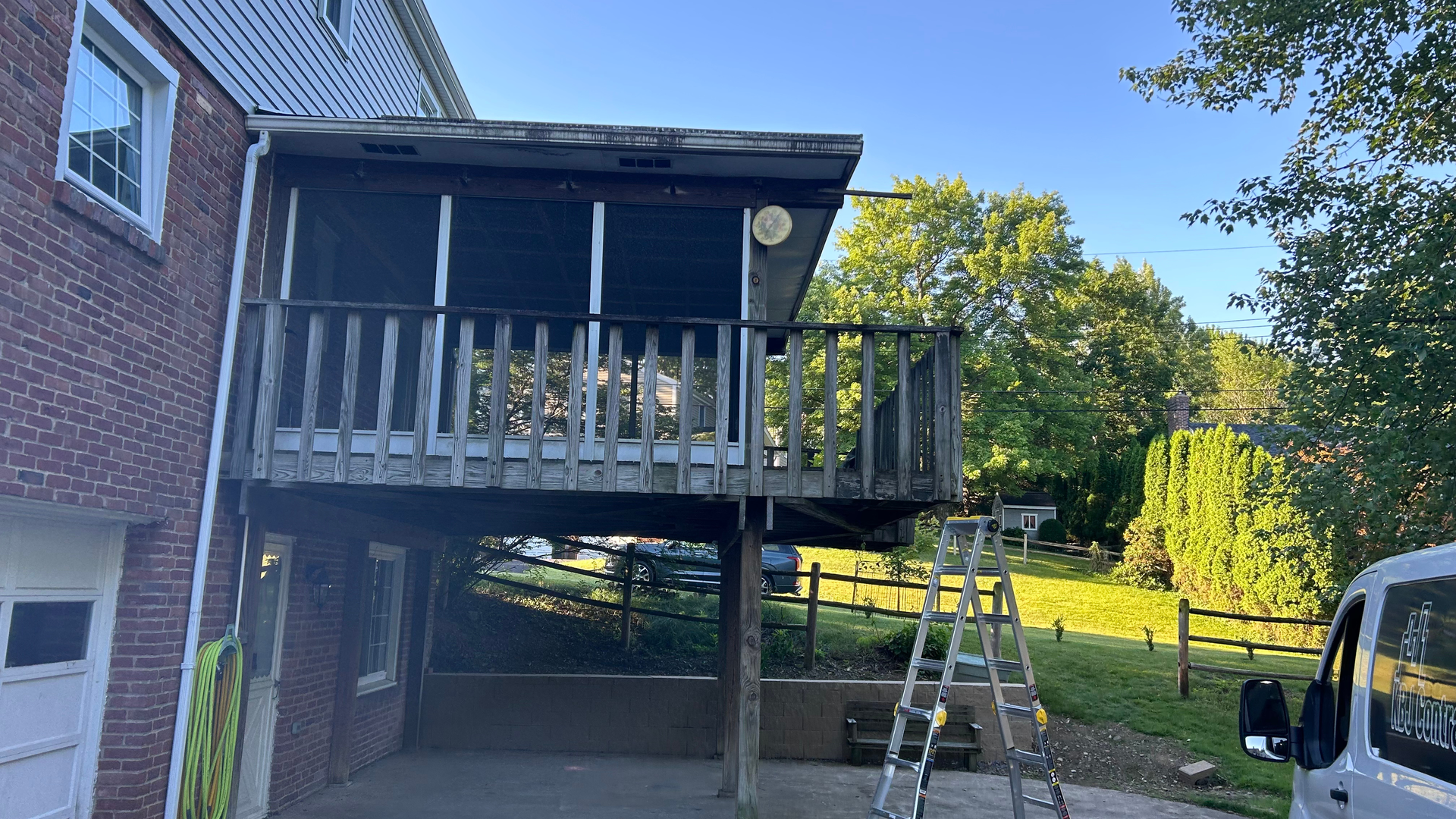 Back deck with wooden railing and stairs beside a brick house, with a ladder leaning nearby