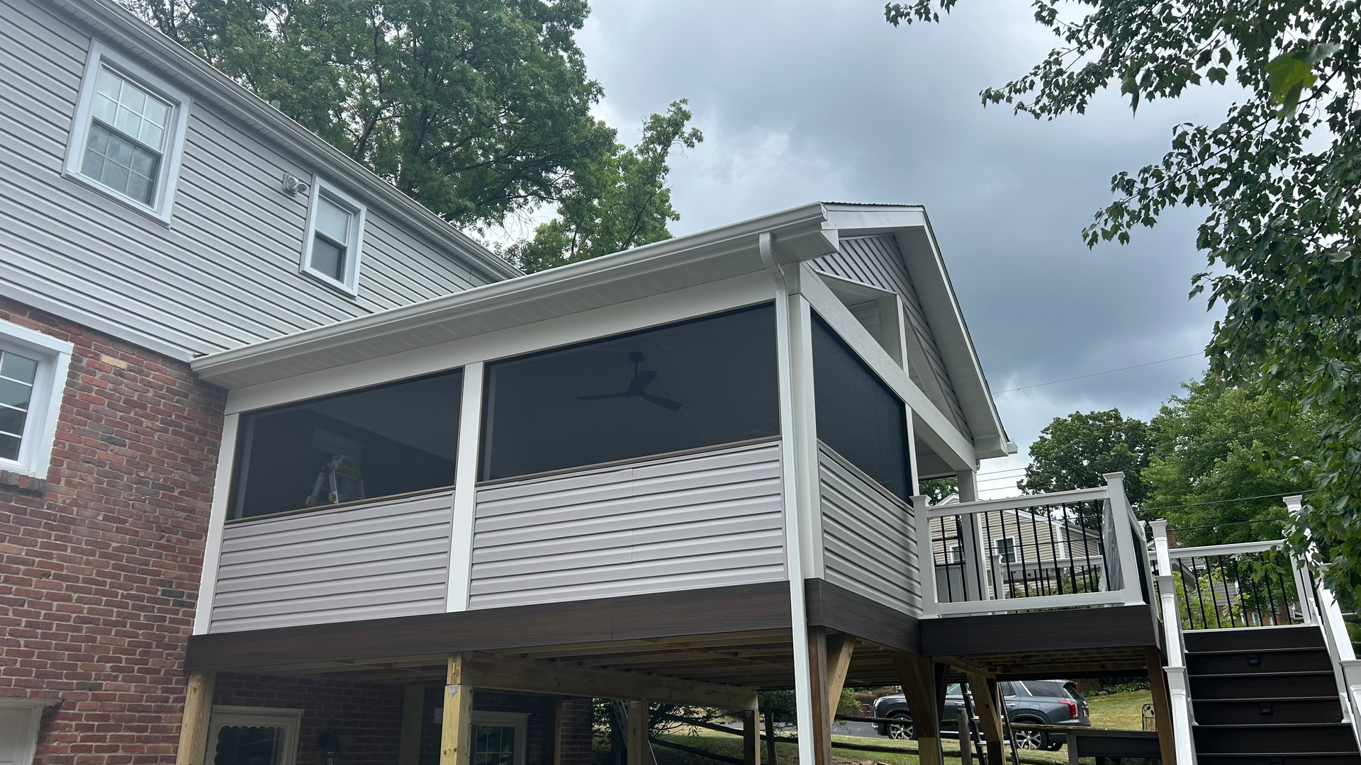 Raised backyard deck with white railings and lattice skirting attached to a brick house under trees
