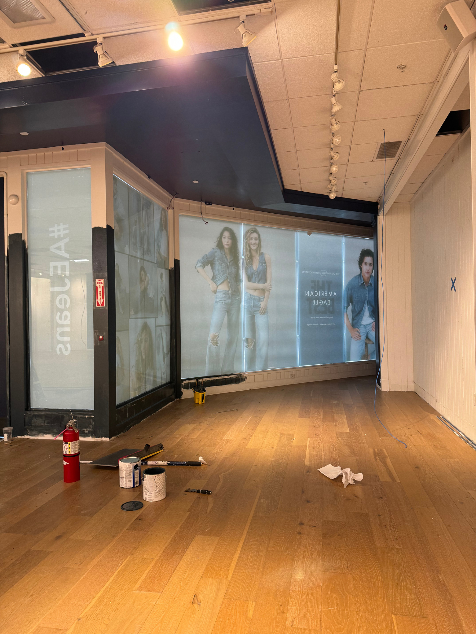 Empty retail store with wooden floor, black walls, and fashion posters along the back wall.