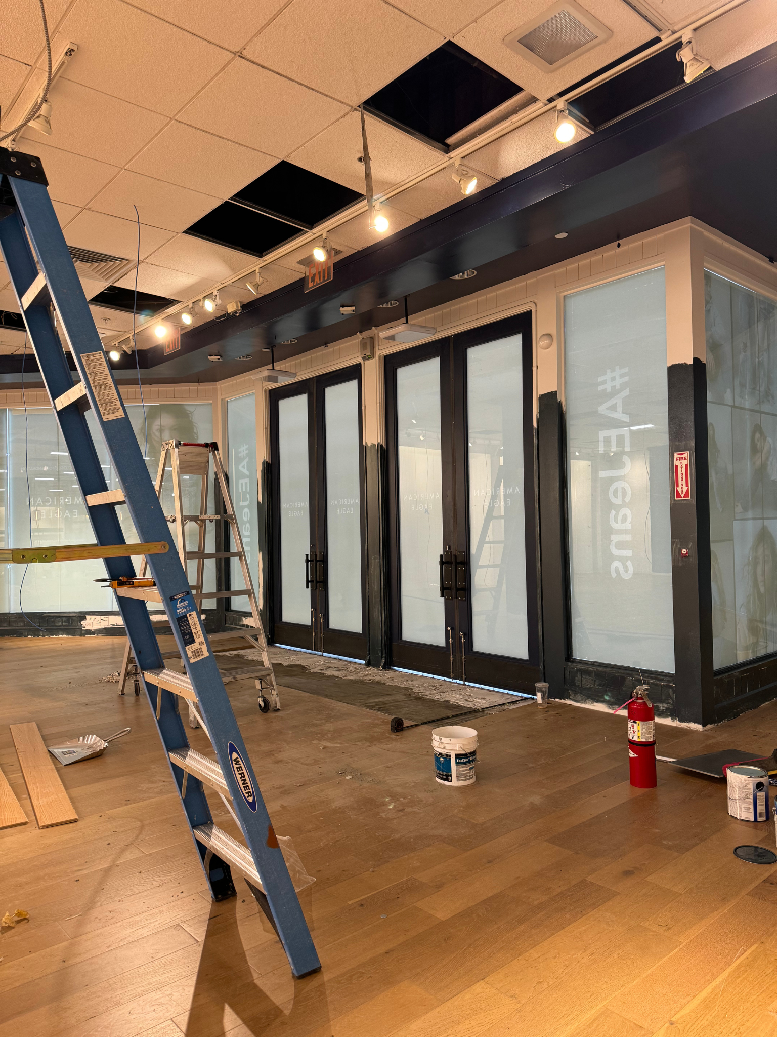 Interior under renovation with ladder, ceiling tiles removed, and frosted glass office doors.