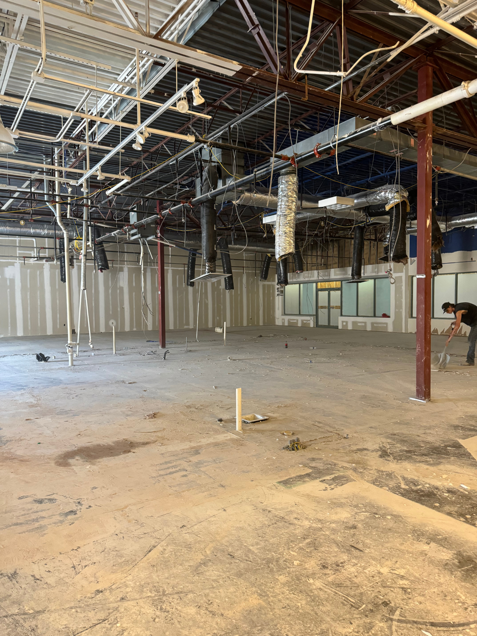 Empty unfinished industrial interior with exposed ceiling pipes, beams, and rough concrete floor