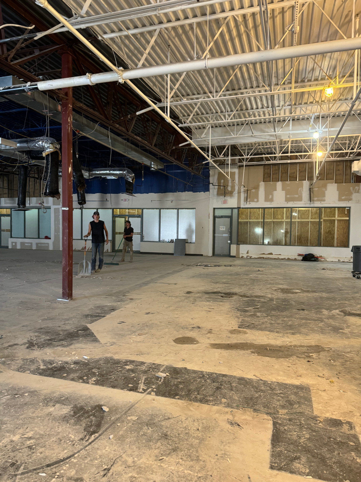 Vacant industrial interior with exposed ceiling, concrete floor, and a few people near the back wall