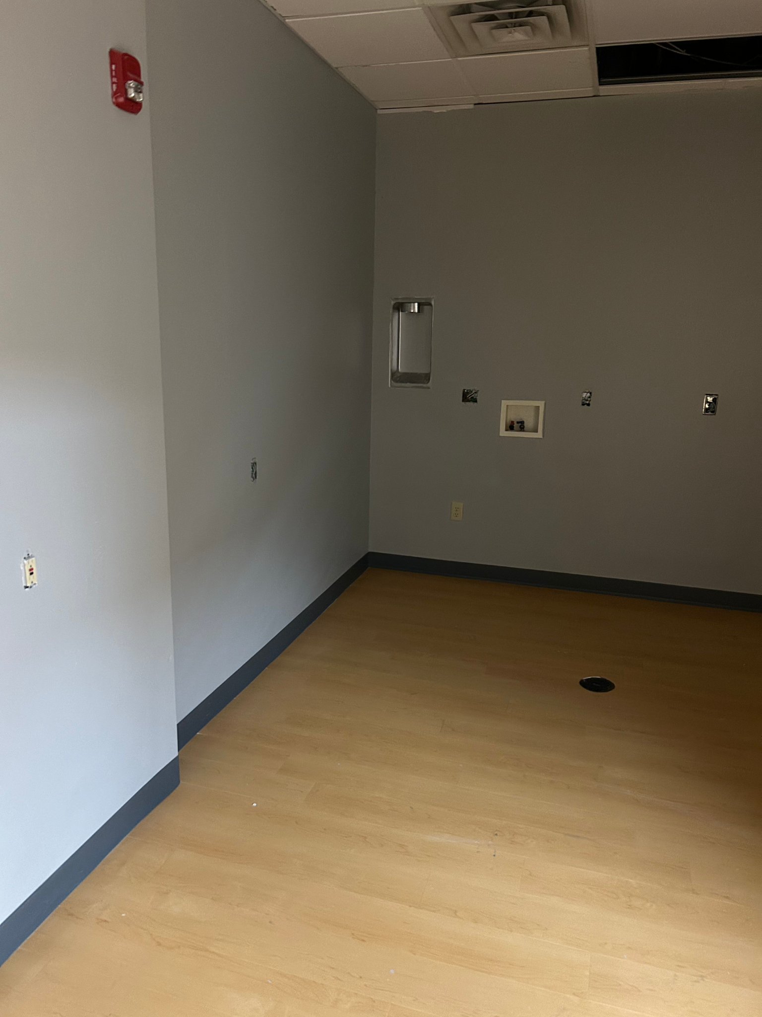 Empty room with gray walls, light wood floor, and ceiling tiles
