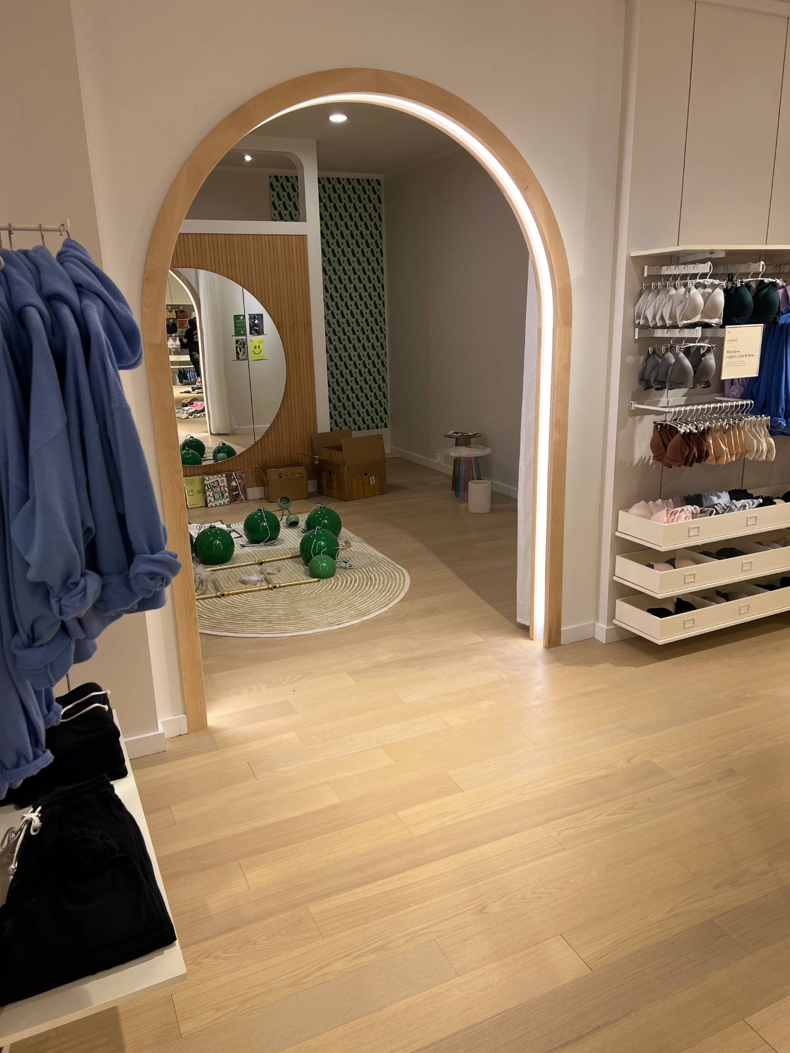 Retail clothing store interior with arched doorway, blue garments on racks, and green decor on the floor.