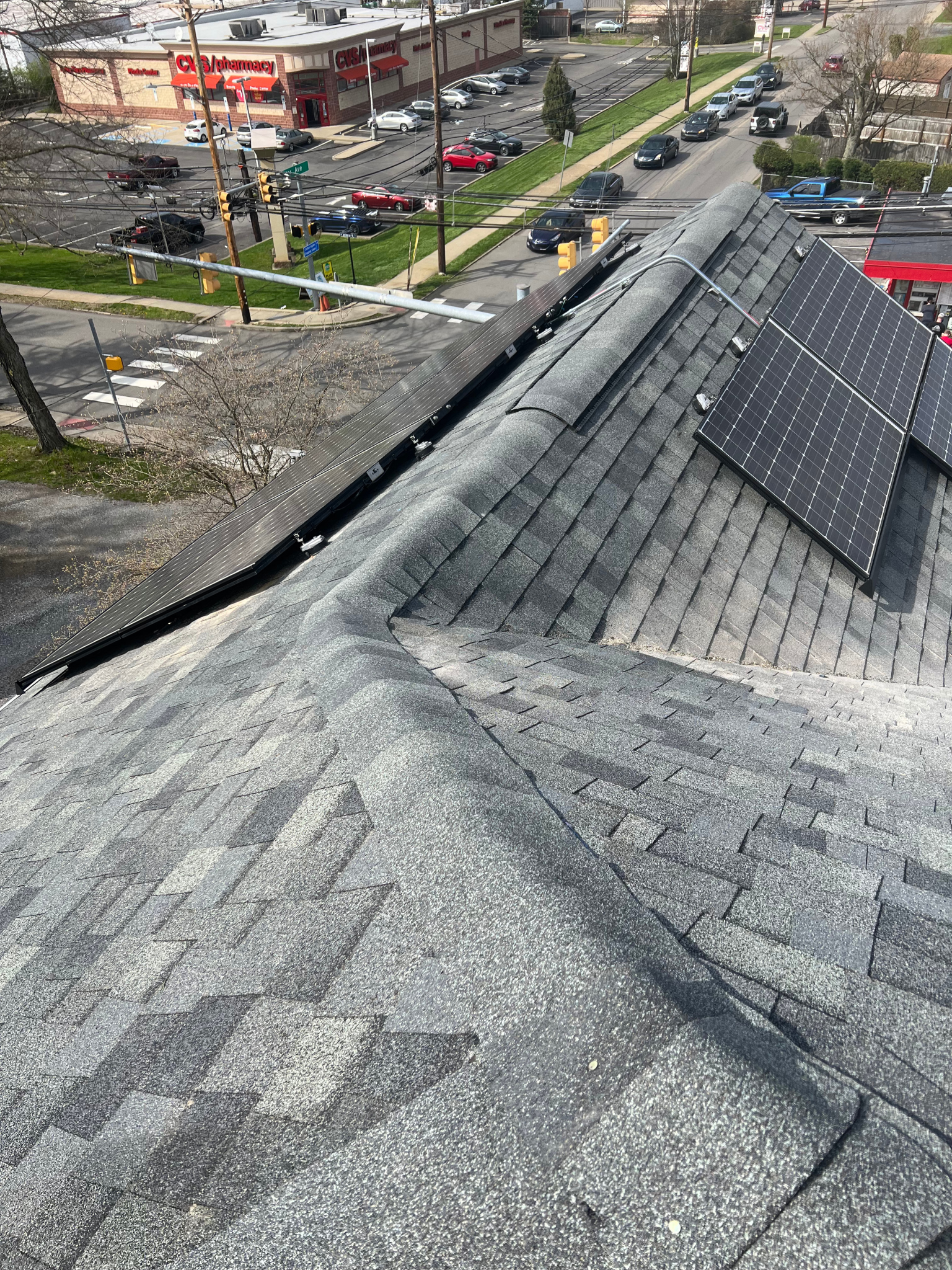 Rooftop with dark shingles and solar panels overlooking a busy street and parking lot.