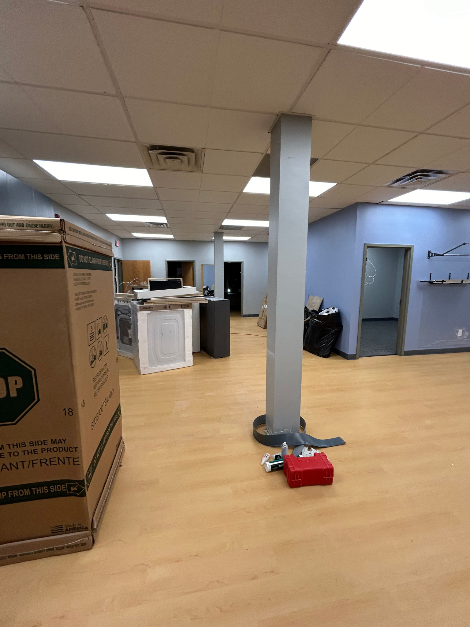 Office room with dropped ceiling, boxes, desk, blue walls, and a gray support column on wood floor.