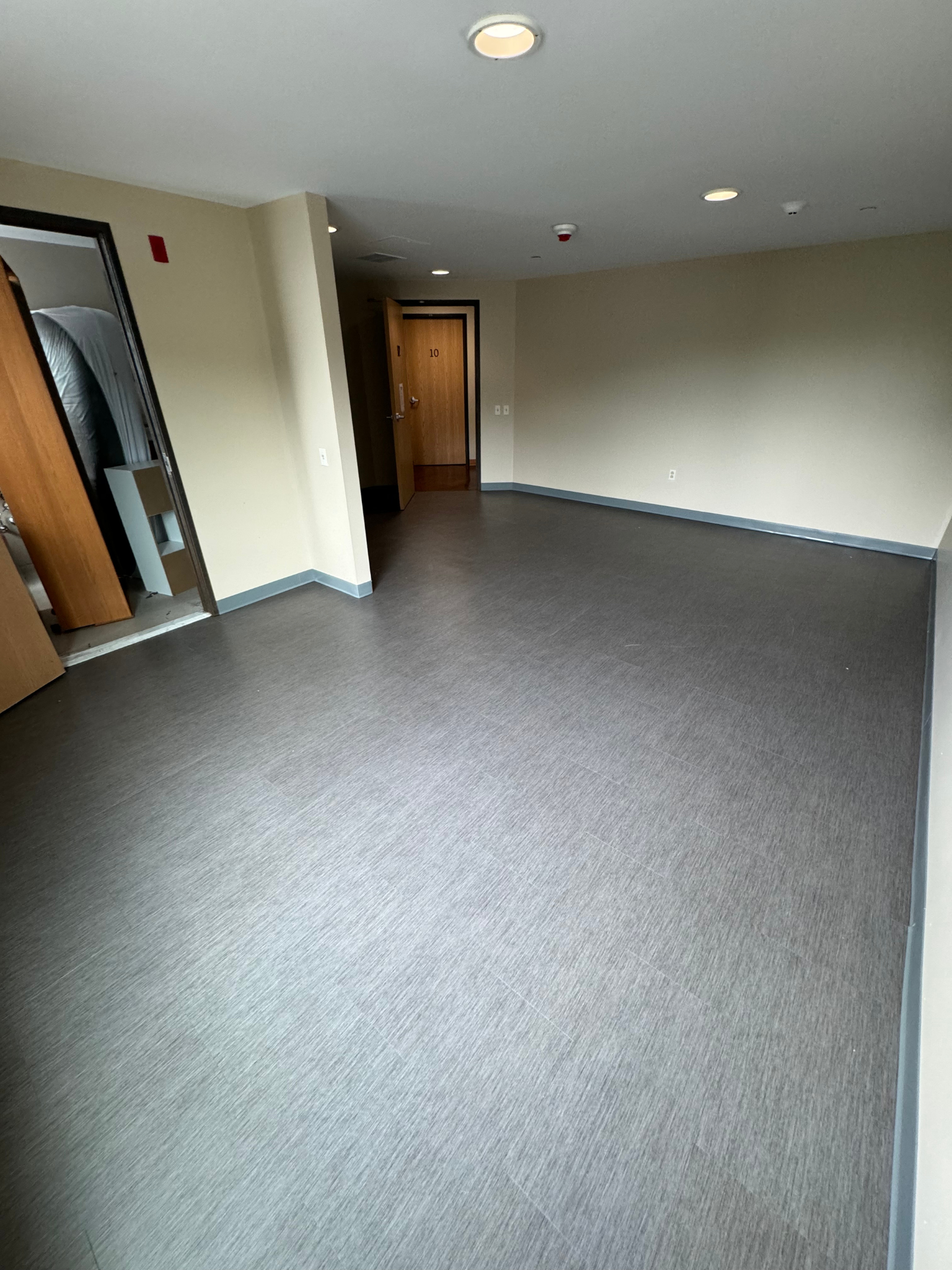 Empty carpeted room with gray walls, ceiling lights, and an open doorway.