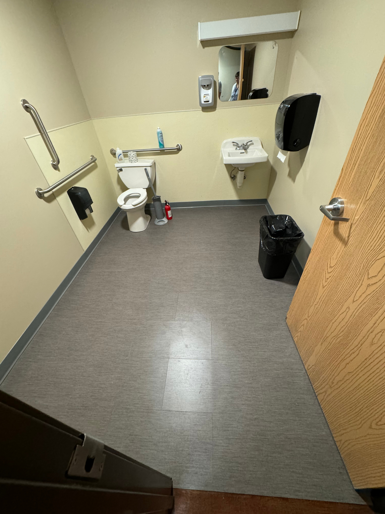 Accessible restroom with toilet, sink, wall grab bars, and gray floor tiles.